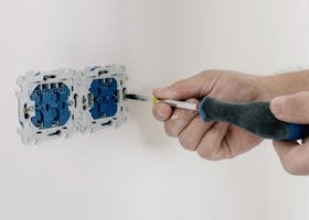 Close-up of hands using a screwdriver to install electrical sockets on a white wall.
