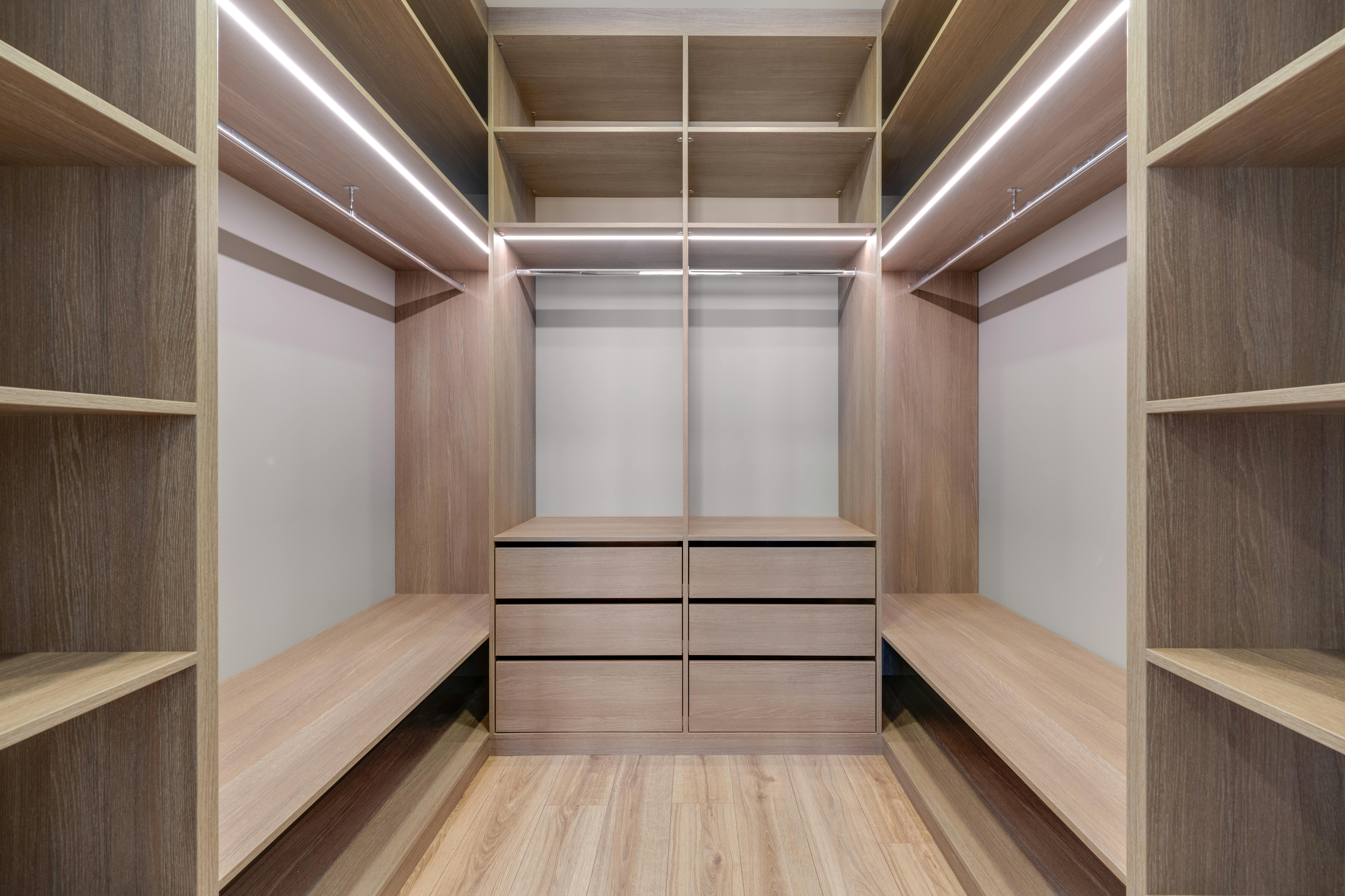 Spacious walk-in closet with wooden shelves and LED lighting creates a minimalist and modern design.